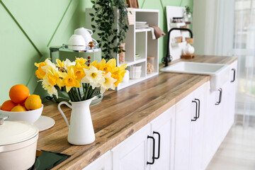 Stylish kitchen counter and daffodil flowers in vase. Closeup
