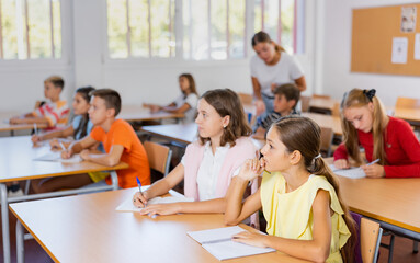 Fototapeta premium Group of preteen schoolchildren diligently working in class, making notes of teacher lecture..