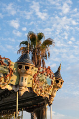 Detail of a vintage carousel with ornate decorations and a palm tree in the background, captured in Cassis, France