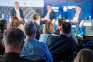 Audience attentively watching a business panel discussion during a professional conference. Engaged participants viewing speakers on stage.