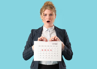 Shocked businesswoman with menstrual calendar on blue background