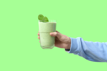 Female hand with glass of fresh spinach smoothie on green background