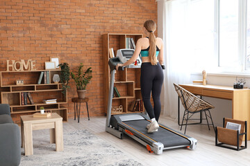 Fototapeta premium Sporty woman on treadmill training at home, back view