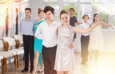 Enthusiastic friendly teenagers, boy and girl in party attire performing elegant waltz in pair in...