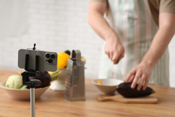 Young man with fresh vegetables recording cooking video in kitchen
