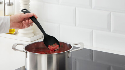 Closeup of a person steering a cooking pot of tomato sauce.