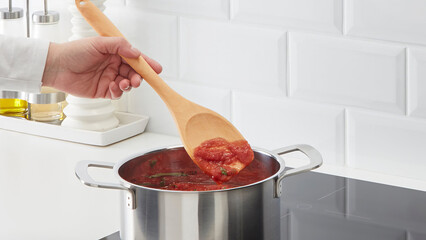 Closeup of a person steering a cooking pot of tomato sauce. © Carterson