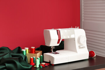 Modern sewing machine with tailor's supplies on red background