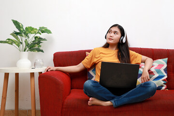 young cute girl uses laptop on soft comfortable sofa and dreams, pensive woman is typing online on computer and thinking on red couch on white isolated background