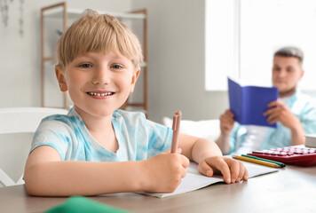 Cute boy taking dictation by his father in room