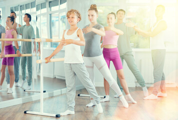 Obraz premium Man coach conducts ballet rehearsal for teenagers. Children hold on to ballet bare and perform exercises, do repetitions of batman figure, rehearse in studio