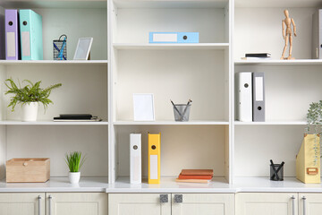 White shelving unit with different stationery and houseplants in office