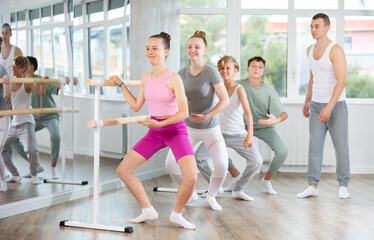 Teenagers doing ballet at group training session in the studio performs demi plie near the ballet barre, standing in a ballet stance © JackF