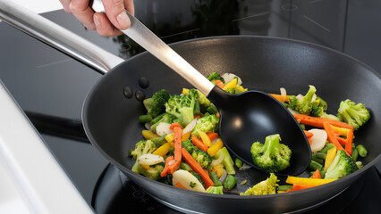 Closeup of a person steering veggeis in a frying pan. © Carterson