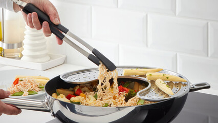 Closeup of a person steering a cooking pot of pasta and veggies. © Carterson