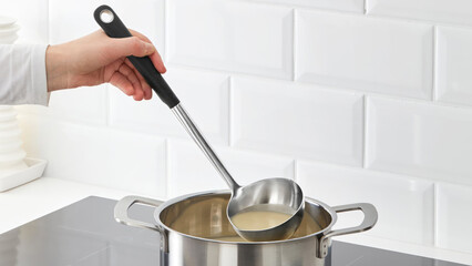 Closeup of a person steering soup in a cooking pot. © Carterson