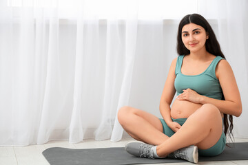 Young pregnant woman sitting on yoga mat in gym