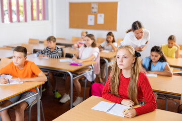 Smart caucasian girl studying in classroom with pupils. Girl exercising during lesson in school.