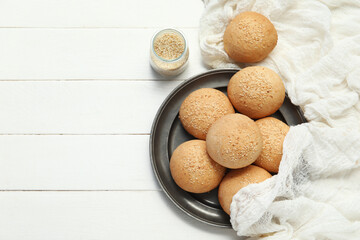 Plate of fresh buns with sesame seeds on white wooden background