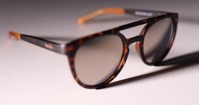 Unisex sunglasses on white background appearing from the dark. Movement of the shadow. Play of light. 