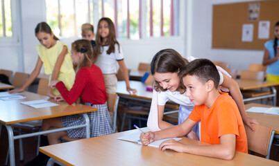 Fototapeta premium Young girls and boys performing tasks in school together, writing in copybook.