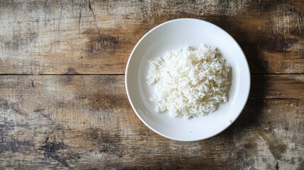 A serving of cooked Jasmine rice on a white plate, resting on a rustic wooden table. Simple and classic Asian cuisine presentation.