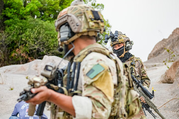 Fototapeta premium A group of military men in combat gear patrol in the middle of a desert and tropical jungle. Soldiers in full combat gear in dry weather conditions assemble and march on a mission.