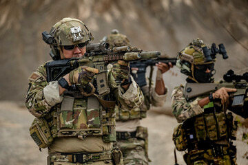 A group of military men in combat gear patrol in the middle of a desert and tropical jungle....