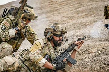 A group of military men in combat gear patrol in the middle of a desert and tropical jungle....
