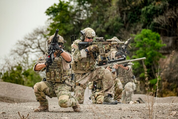 A group of military men in combat gear patrol in the middle of a desert and tropical jungle....