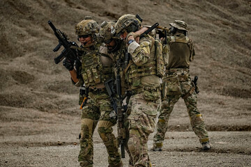 A group of military men in combat gear patrol in the middle of a desert and tropical jungle. Soldiers in full combat gear in dry weather conditions assemble and march on a mission.