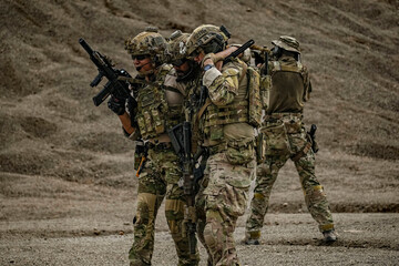 Fototapeta premium A group of military men in combat gear patrol in the middle of a desert and tropical jungle. Soldiers in full combat gear in dry weather conditions assemble and march on a mission.