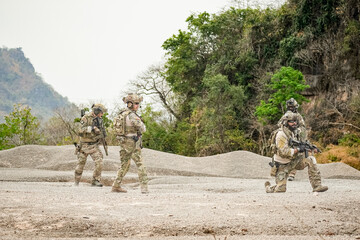 A group of military men in combat gear patrol in the middle of a desert and tropical jungle....