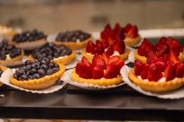 A tray of blueberry and strawberry tarts. The blueberries are whole and the strawberries are sliced. There's a cream center and golden baked crust. The individual pies are on round white paper.