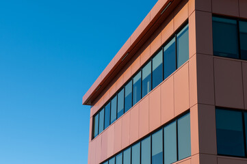 The exterior of a modern style building with multiple rows of windows and contemporary style aluminum metal composite panels.  The background is blue sky and the sky is reflected in the windows.