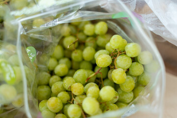 A bunch of sour green grapes on stems in a clear plastic bag. The fresh grapes are for sale at a...