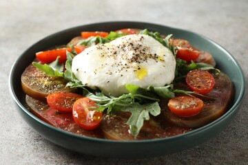 Delicious fresh burrata salad in bowl on gray textured table, closeup
