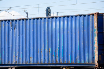 blue shipping container on a train, showing signs of wear and rust, symbolizes global commerce and the intricate logistics network that connects markets worldwide in a multimodal environment.