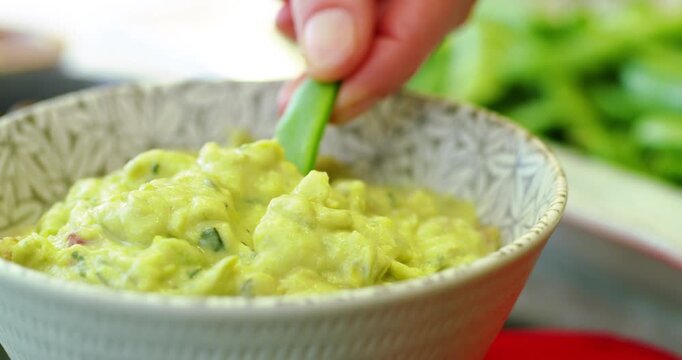 Hand dips snap pea into dip close up