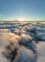 Aerial view from above at high altitude of dense puffy cumulus clouds flying in evening. Amazing sunset from airplane window point of view