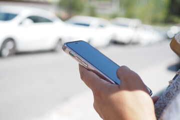 A person is utilizing their smartphone while outdoors, in a busy urban environment nearby