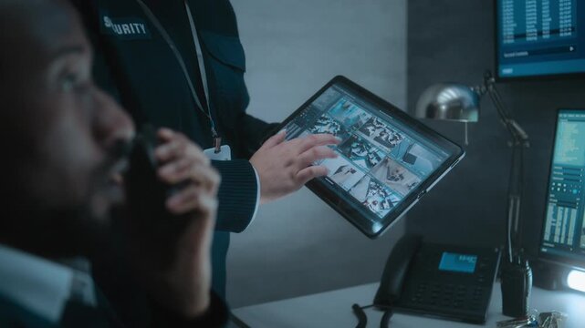Female employee shows CCTV footage to African American male security officer using tablet computer. Diverse security operators control surveillance cameras on computer monitors in monitoring center.