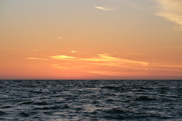 Dramatic bright red sky at ocean sunset, soft evening clouds over sea dark water