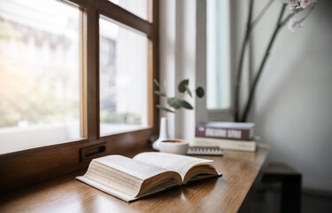 An open book for reading and relaxing with coffee drink on wooden table by the window in cafe