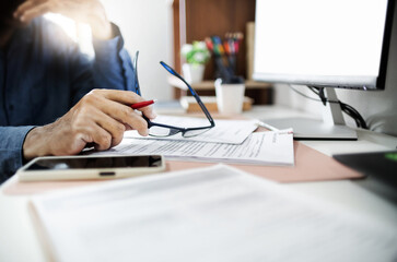 Tired exhausted businessman holding eyeglasses sitting in home office with computer and many...