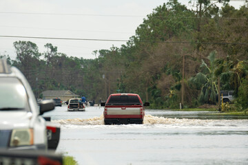 Flooded road in Florida after heavy hurricane rainfall. Evacuating cars and surrounded with water houses in suburban residential area.