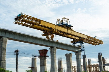 Large yellow launching gantry crane on top of elevated concrete pillars, used in bridge or railway...