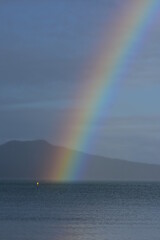Overcast sky and grey sea with rainbow over Rangitoto volcano island. Location: Auckland New Zealand