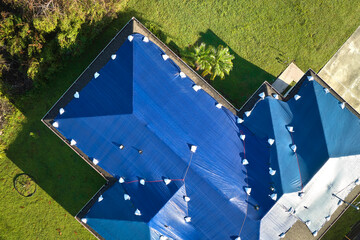 Top view of leaking house roof covered with protective tarp sheets against rain water leaks until...