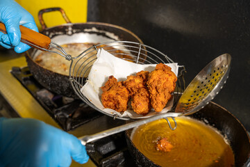 Cook removing breaded fried chicken from deep fryer basket